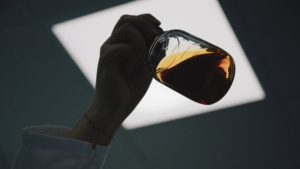 Bitterschwarzer Puderzucker wird in einem Glas mit brauner Flüssigkeit auf einem dunklen Hintergrund gehalten.